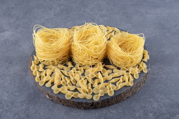 Two types of raw pasta on wood piece.