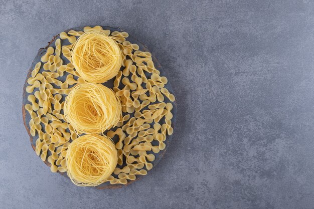 Two types of raw pasta on wood piece.