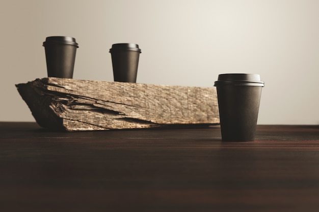 Two unfocused black take away paper cups with closed caps isolated on wooden brick on table