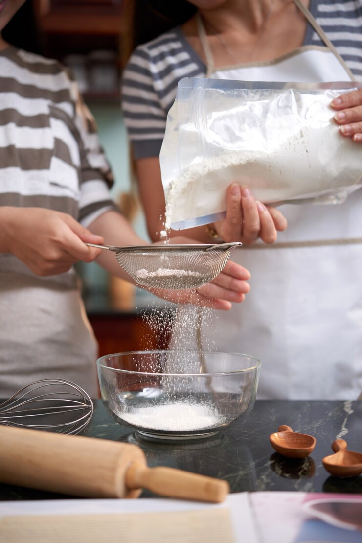 Free Photo two unrecognizable women pouring flour into sieve in kitchen at home
