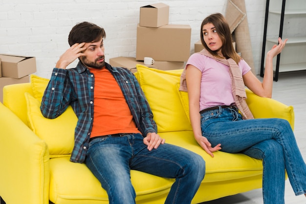 Две расстроенные молодая пара сидит на желтом диване в своем новом доме