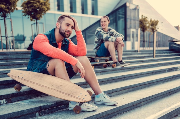 Free photo two urban males posing with longboard on steps in downtown.