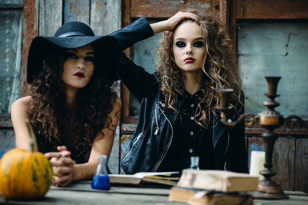 Free photo two vintage witch sitting at the table in an abandoned place on the eve of halloween