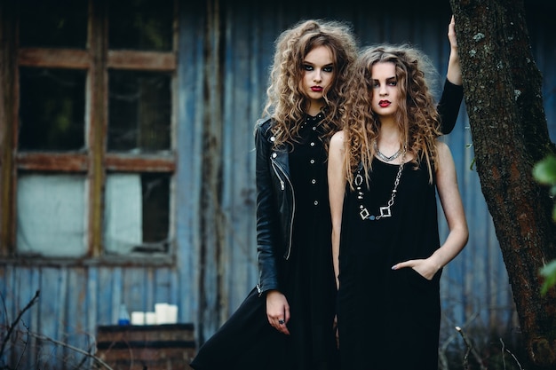 Two vintage women as witches, posing beside an abandoned building on the eve of Halloween