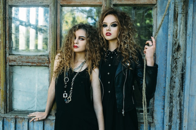 Two vintage women as witches, posing beside an abandoned building on the eve of Halloween