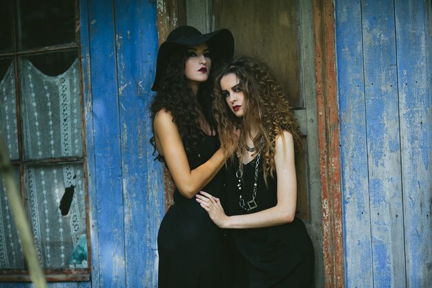 Two vintage women as witches, posing beside an abandoned building on the eve of Halloween