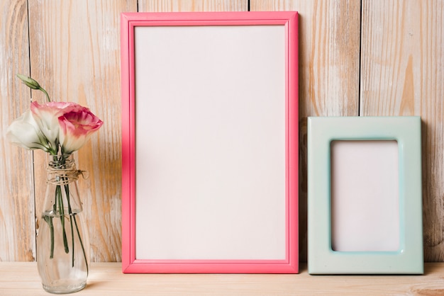 Free photo two white frame with pink and blue border and flower vase against wooden background