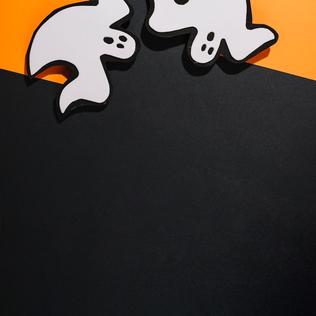 Free photo two white handmade ghosts on orange paper