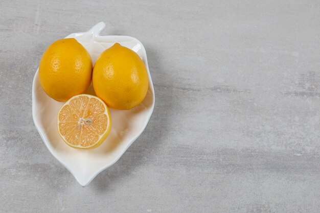 Два целых с половиной лимона в тарелке на мраморной поверхности