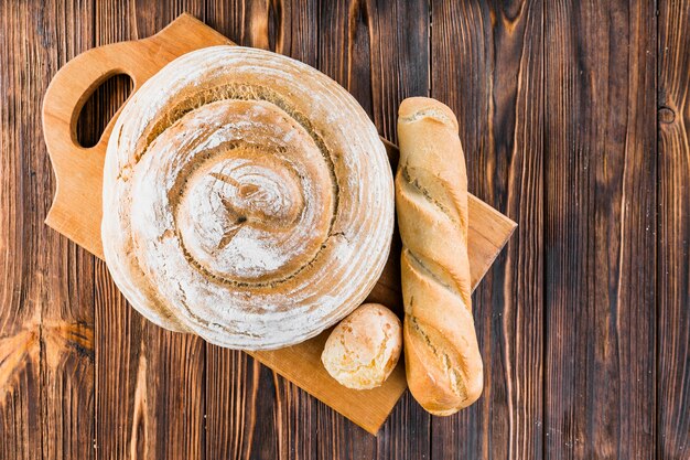 Foto gratuita due intere rotonde di pane e baguette sul tagliere sullo sfondo in legno