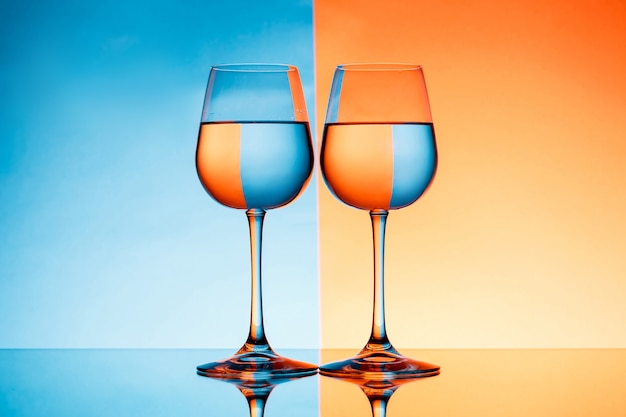 Two wineglasses with water over blue and orange background.