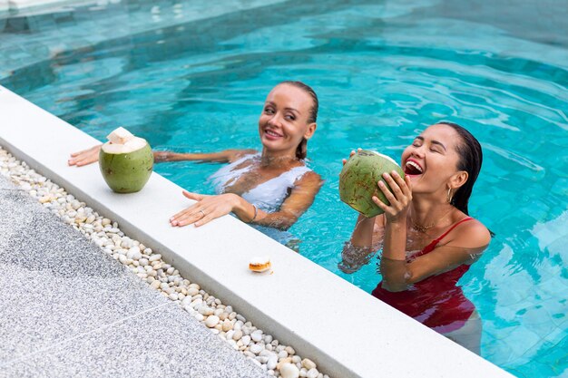 Two woman friends asian and caucasian with makeup in swimming pool at villa