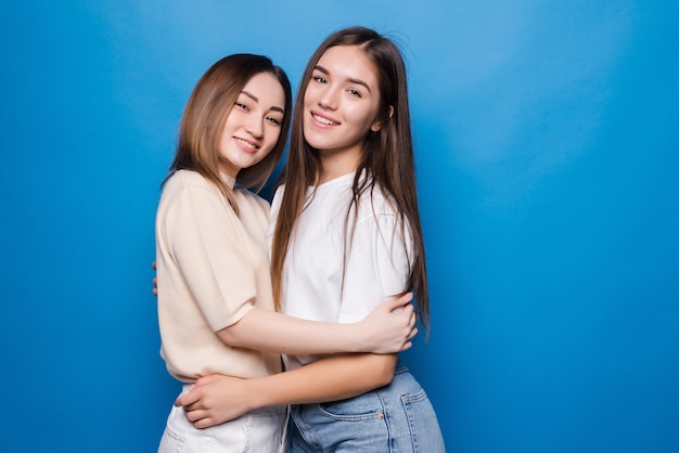 Two woman friends hug each other isolated blue color wall