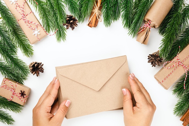 Two woman hands hold paper craft envelope decorations from christmas tree branches and gift boxes on...