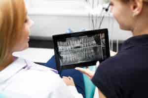 Free photo two woman look at the tooth picture on a tablet at dentist office