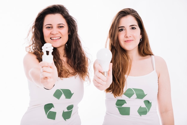 Two woman wearing recycle icon tanktop showing fluorescent bulb and led bulb