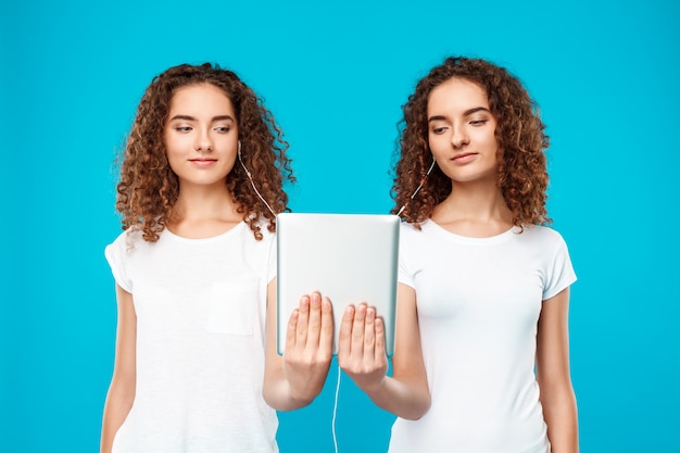 Free photo two womans twins looking at tablet, smiling over blue.