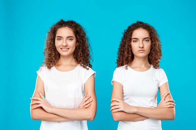 Two womans twins posing with crossed arms over blue.