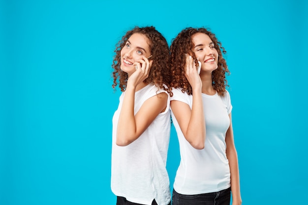 I gemelli di due womans che parlano sui telefoni, sorridenti sopra l'azzurro.