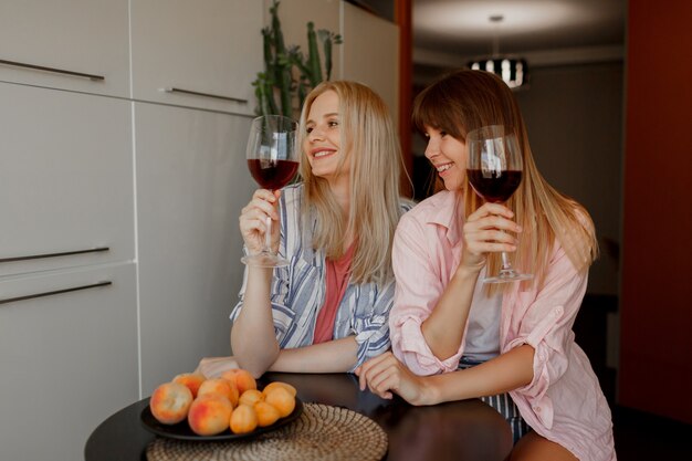 キッチンでワインを楽しむ2人の女性の親友。居心地の良い家庭的な雰囲気。新鮮な果物を盛り付けます。
