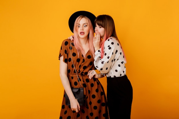 Two women gossiping over yellow wall in stylish vintage outfit