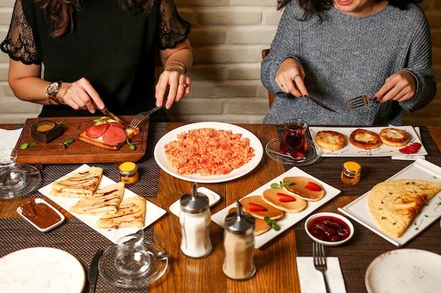 Two women enjoying breakfast with toasts, crepes, pancakes, jam and scrambled eggs