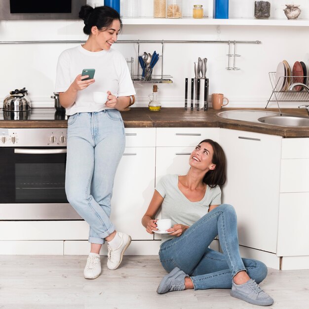 Two women at home in the kitchen chatting over coffee