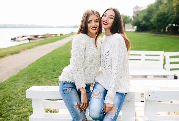 Two women lean on a white bench in the park