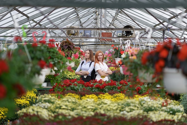 Two women posing in a greenhouse between hundreds of flowers