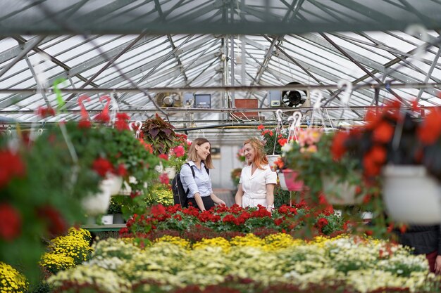 Two women posing in a greenhouse between hundreds of flowers