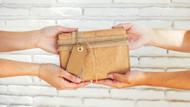 Free photo two women's hand holding birthday gift against brick wall