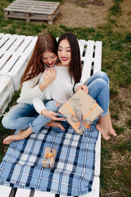 Free photo two women sit on a bench outside and shoot gifts for smartphone