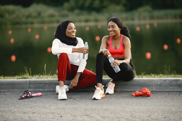 Two women sitting near the lake after doing some workout with dumbbells and jump rope