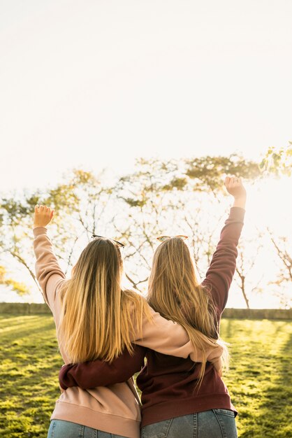 Two women in sunlight hug from behind