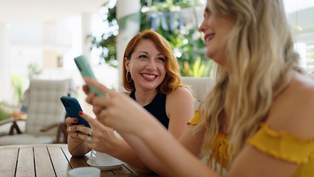 Foto gratuita due donne che usano smartphone e bevono caffè seduti sul tavolo della terrazza di casa