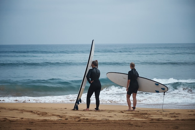 Two women in wetsuits with surfboards are getting ready to go into water on cool summer day