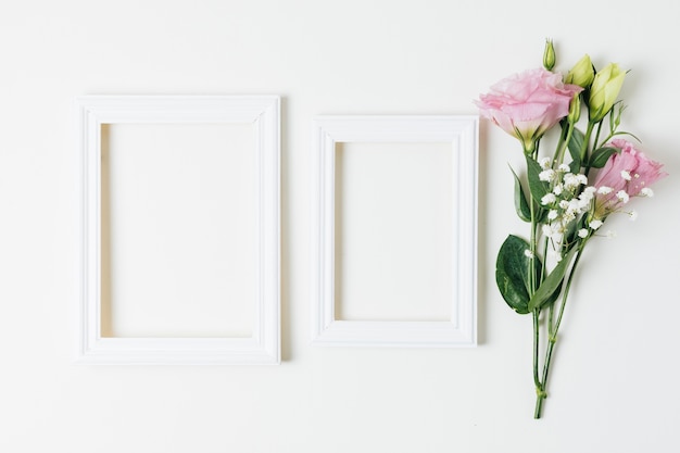 Two wooden empty frames near the pink eustoma and baby's-breath flowers on white background