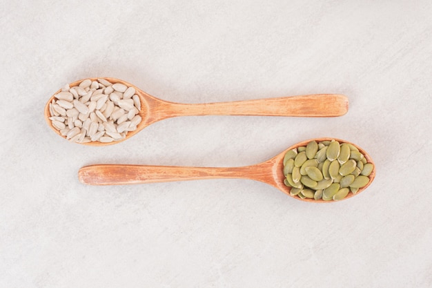 Two wooden spoon of sunflower and pumpkin seeds on white surface.