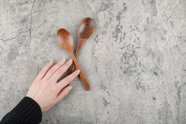 Two wooden spoons and female hand on marble background