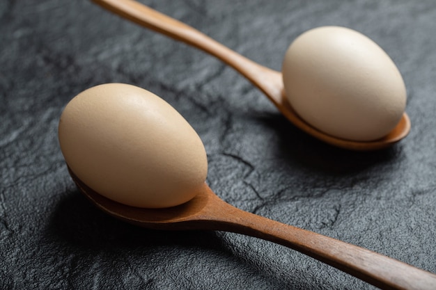 Two wooden spoons of raw eggs on black background