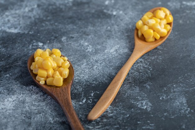 Two wooden spoons of sweet corns on marble.