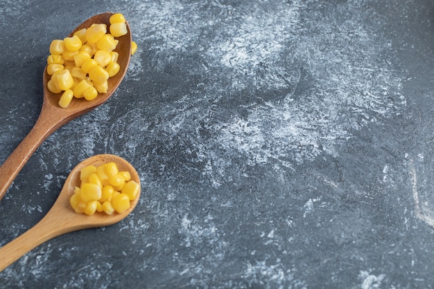 Two wooden spoons of sweet corns on marble.