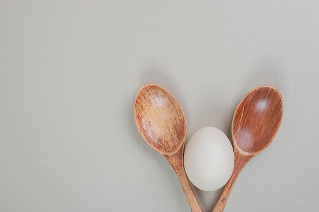 Two wooden spoons with chicken white egg .