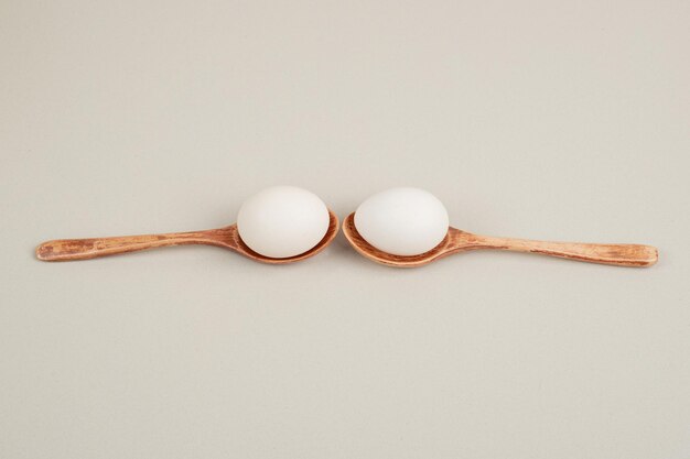 Two wooden spoons with chicken white eggs .