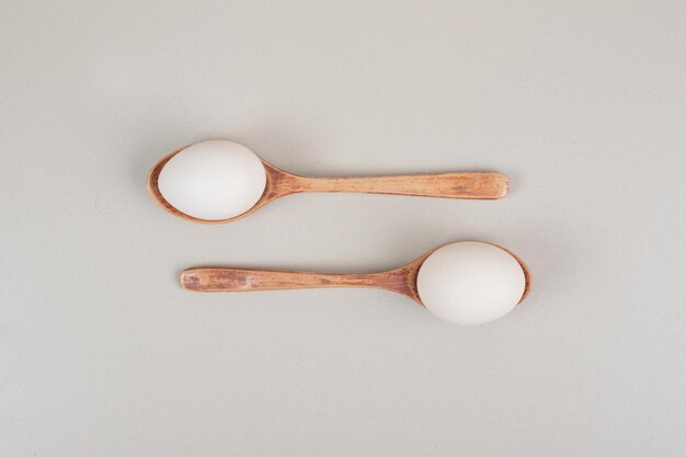 Two wooden spoons with chicken white eggs .