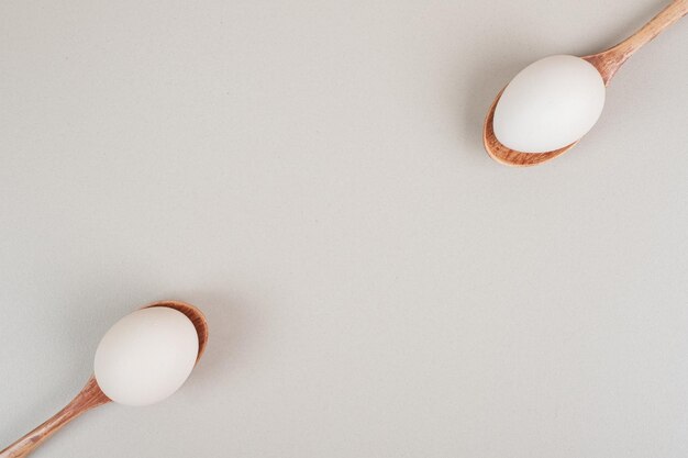 Two wooden spoons with chicken white eggs .