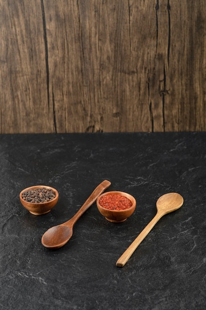 Two wooden spoons with wooden bowls of pepper balls and pepper powder
