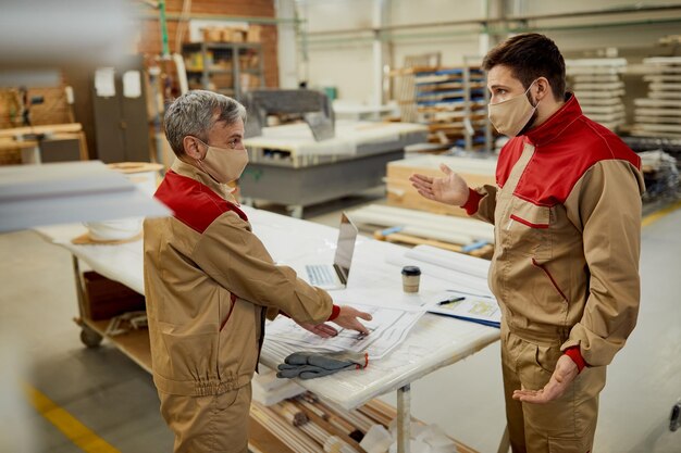 Двое рабочих в масках обсуждают планы проекта в столярной мастерской