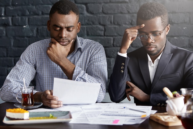 Due uomini d'affari afroamericani preoccupati seri che lavorano attraverso i documenti e che discutono il rapporto finanziario che ha concentrato gli sguardi