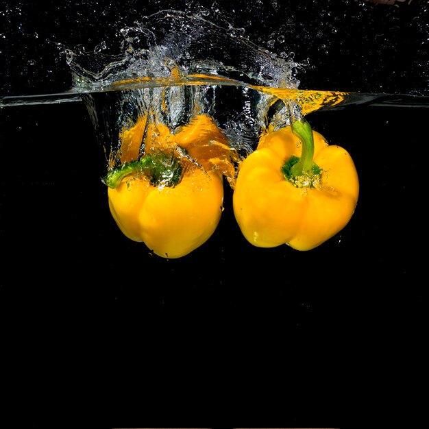 Two yellow bell peppers falling into clear water